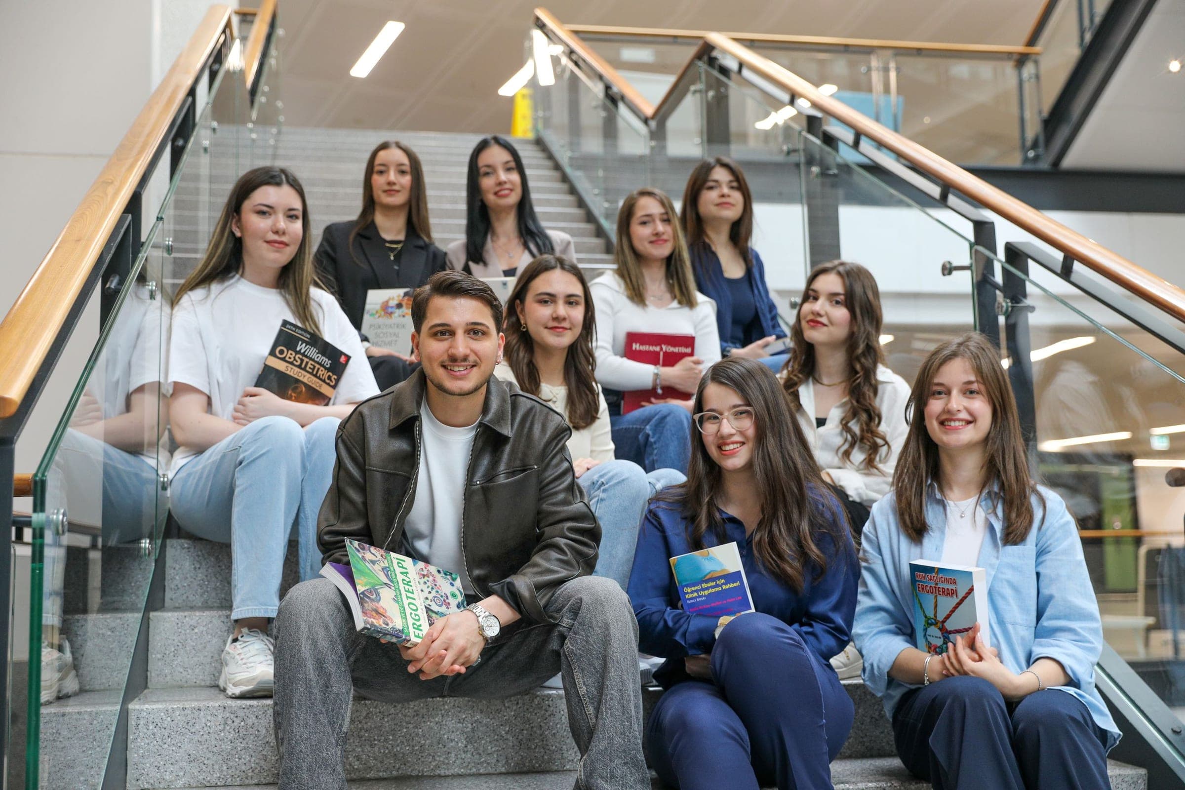 A group of smiling students sitting on a staircase holding books